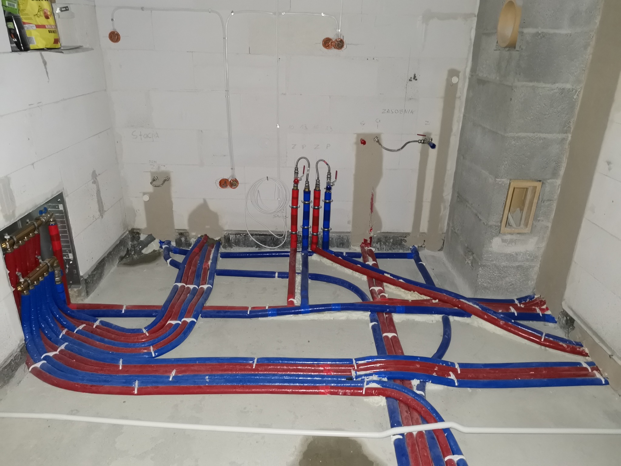 Rozłożona instalacja ogrzewania podłogowego z rurami w kolorze niebieskim i czerwonym, przed wylaniem posadzki, widoczne ściany z betonu komórkowego.
