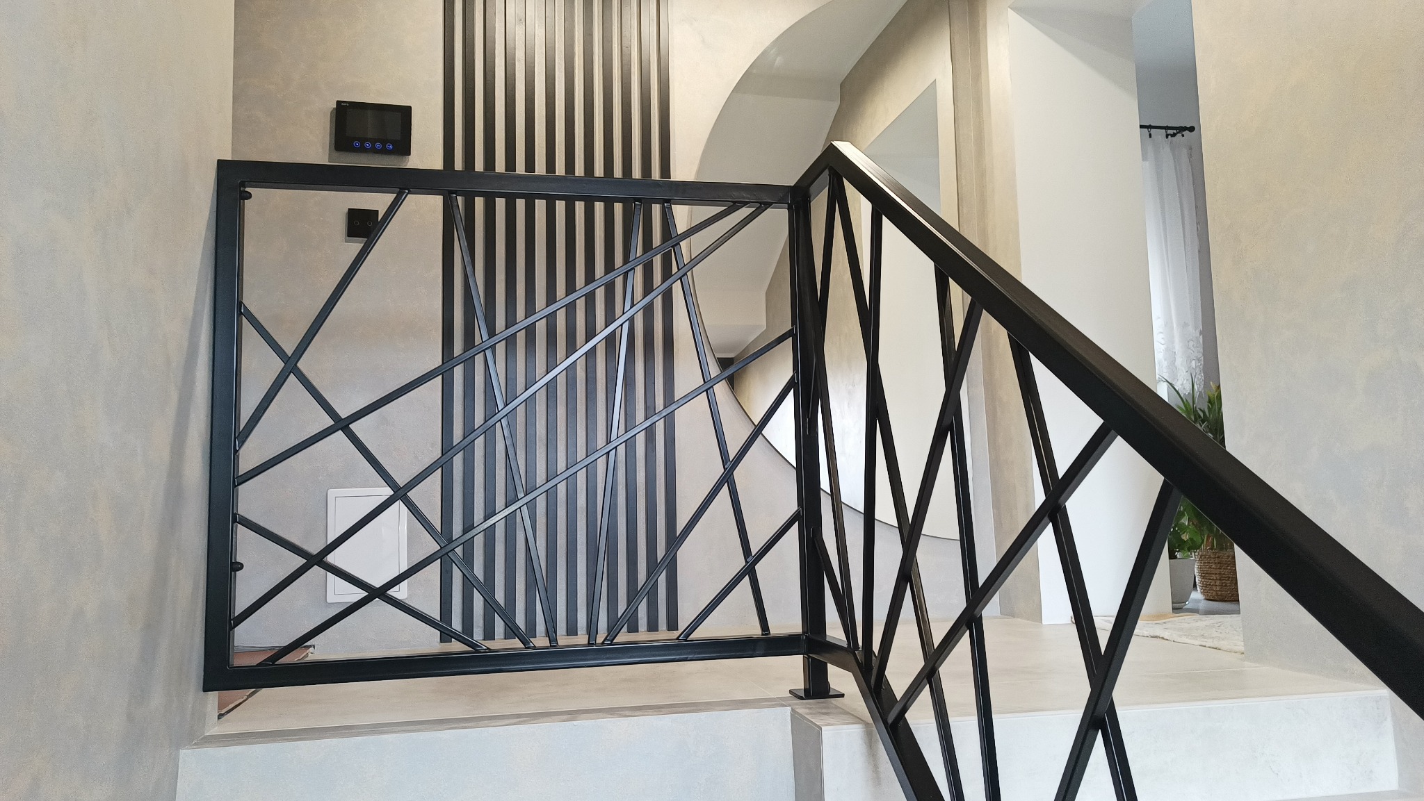 Nowoczesna, czarna balustrada schodowa z geometrycznym wzorem na tle ściany z dekoracyjnymi panelami pionowymi. Minimalistyczny design, jasne wnętrze.