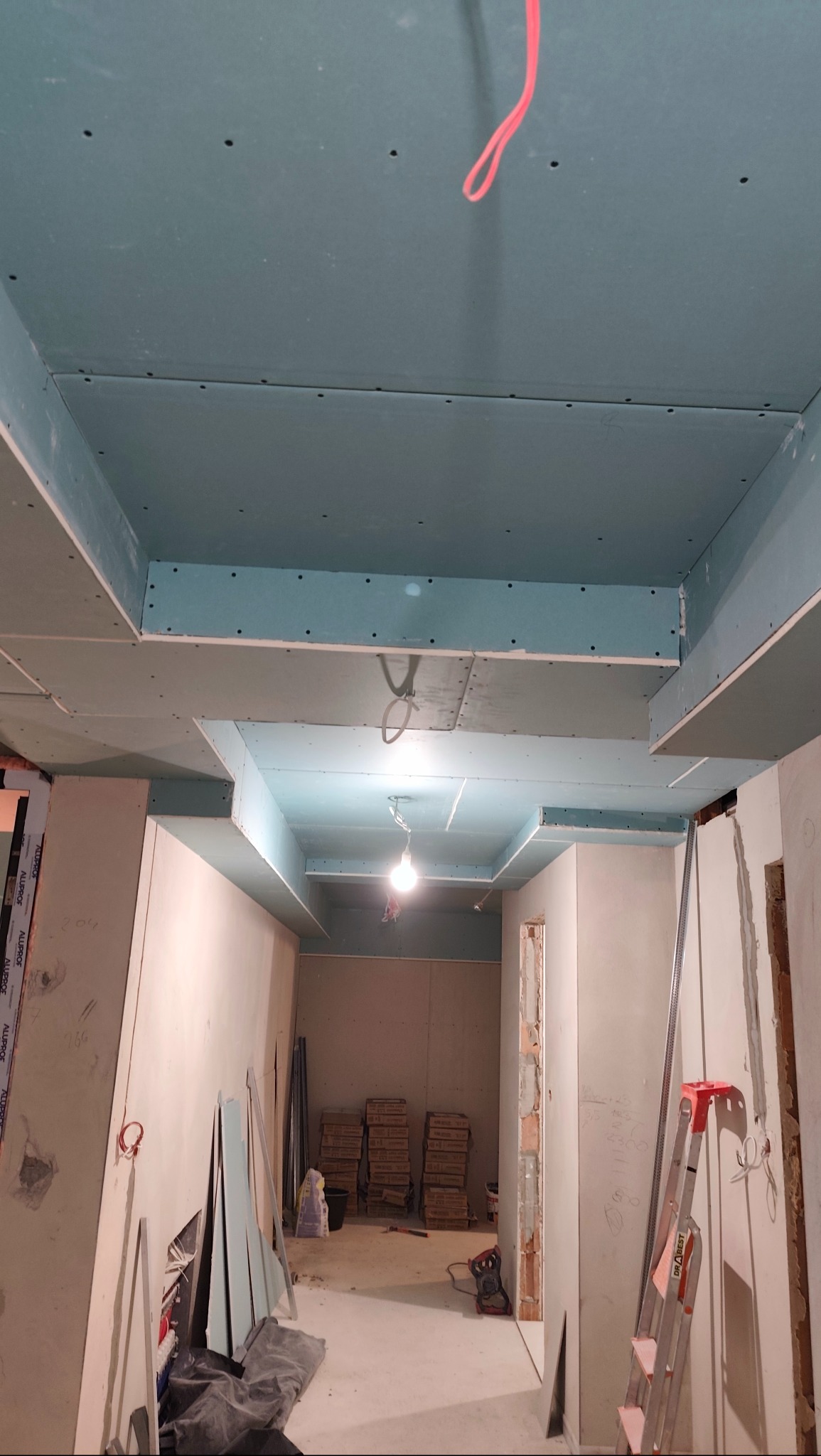 Sufit podwieszany z płyt karton-gips, widoczne łączenia i otwory na śruby, surowy stan wykończenia, wnętrze w trakcie remontu, drabina oparta o ścianę.