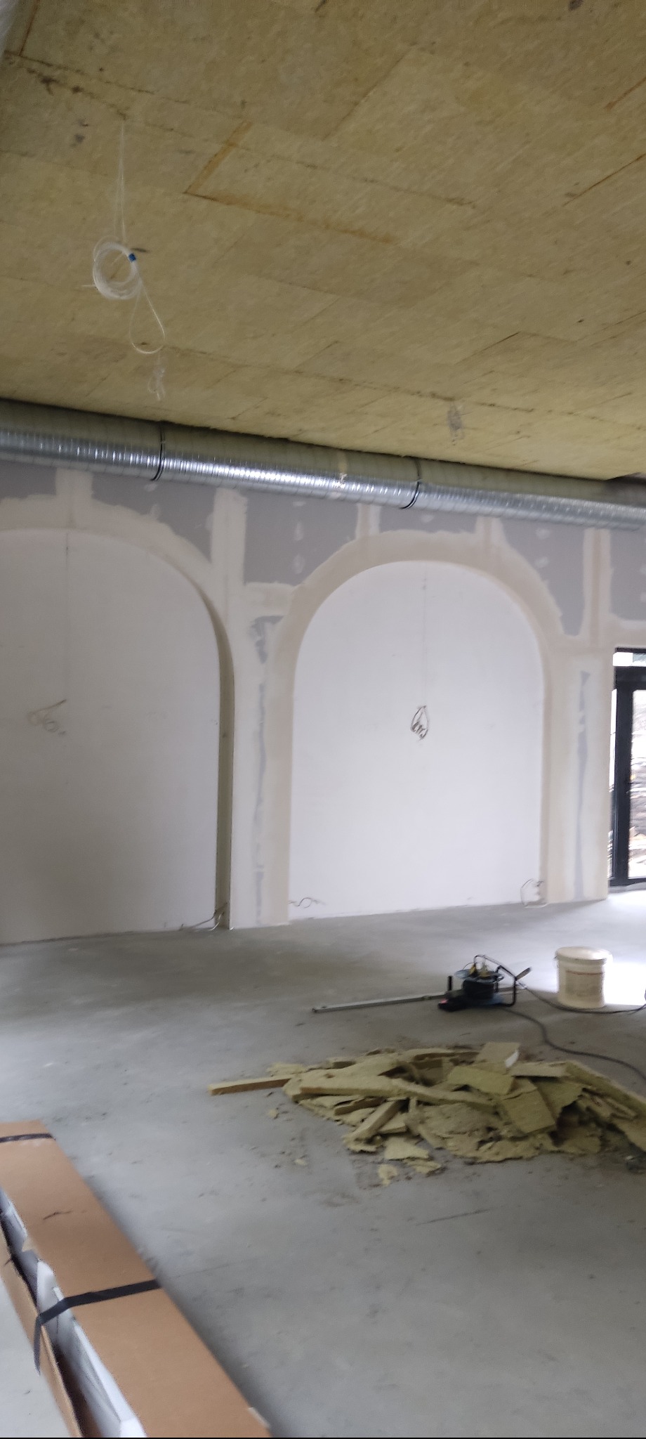 Wnętrze w trakcie prac wykończeniowych: ściany z łukami po szpachlowaniu, widoczne narzędzia i materiały budowlane, sufit z izolacją.