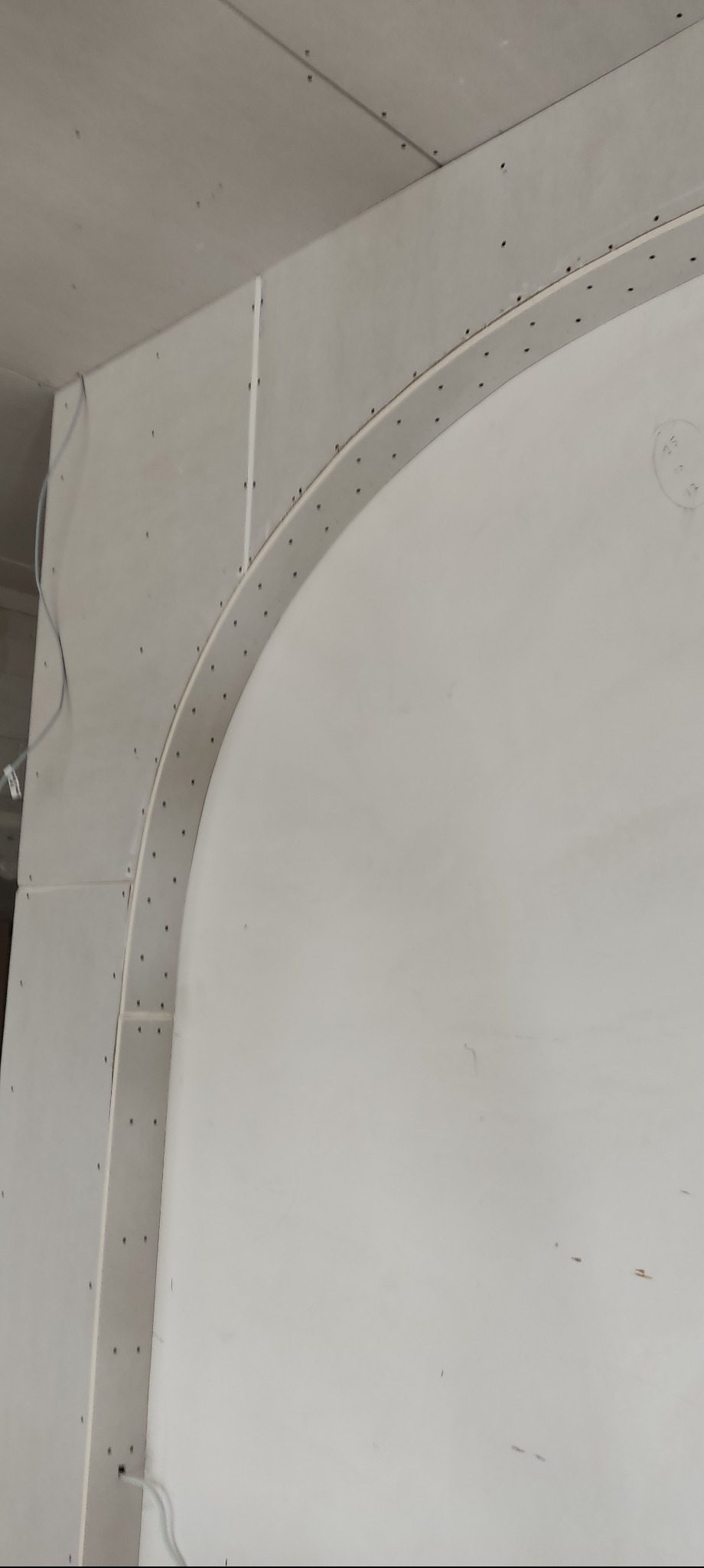 Łuk z płyty karton gips, mocowany do ściany w Żywcu. Widoczne wkręty i fragment sufitu. Praca w trakcie realizacji, surowy stan wykończenia.