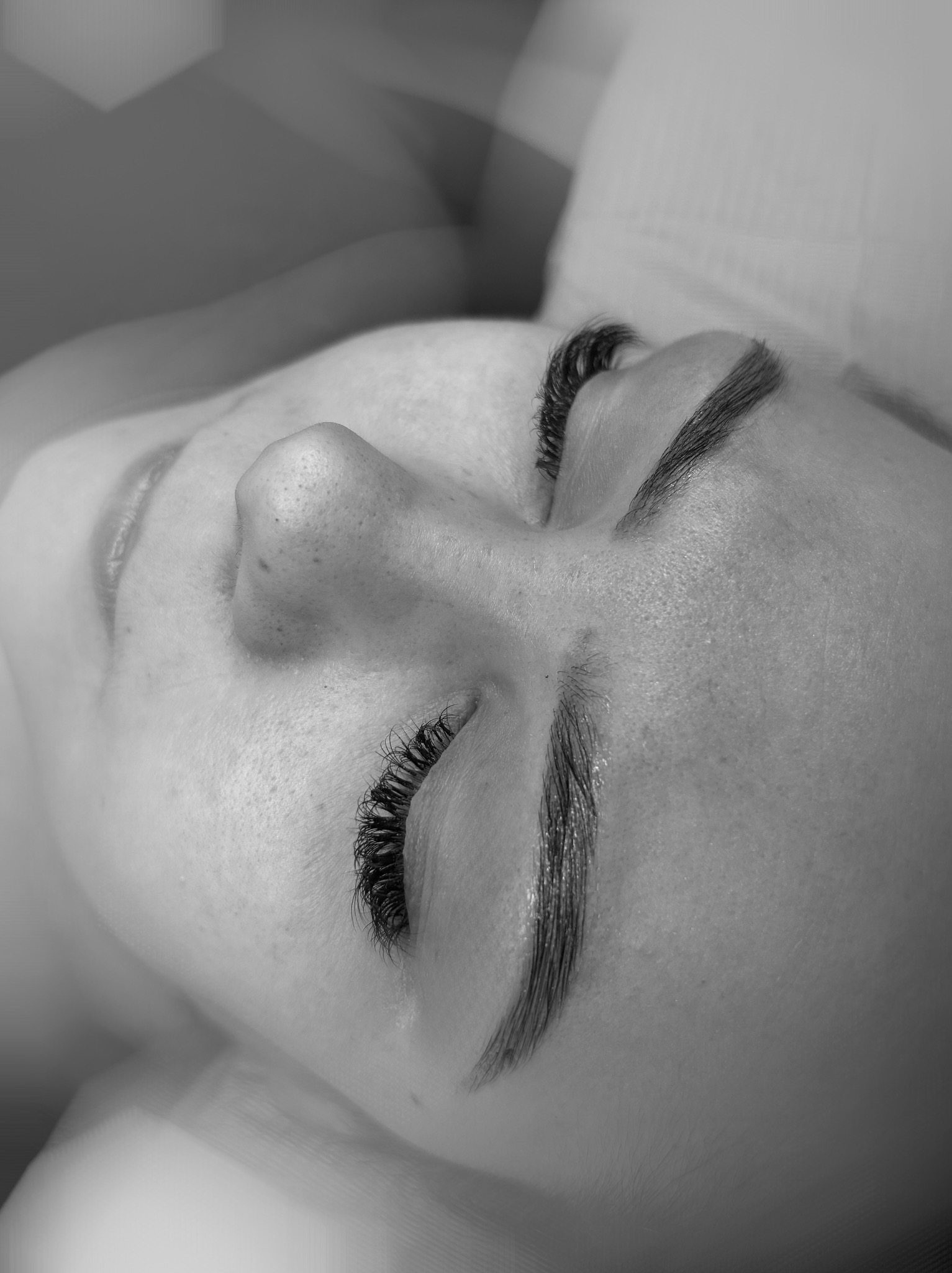 Zbliżenie na twarz kobiety z zamkniętymi oczami, prezentujące efekt przedłużonych rzęs i wyregulowanych brwi w monochromatycznej tonacji.