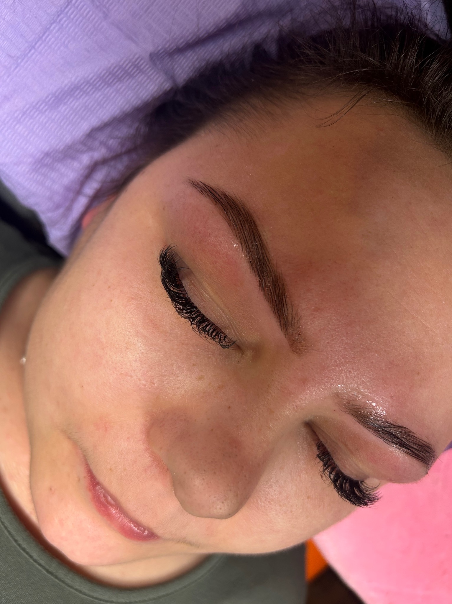 Zbliżenie na twarz kobiety po zabiegu laminacji brwi i przedłużania rzęs. Widoczne perfekcyjnie wystylizowane brwi i długie, gęste rzęsy.