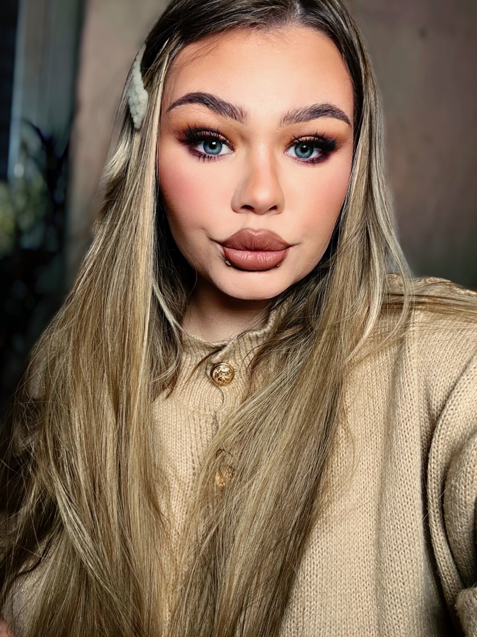 Portret kobiety z pełnym makijażem: wyraziste oko z długimi rzęsami, podkreślone brwi, konturowanie twarzy i usta w odcieniach nude. Włosy blond, spięte ozdobną spinką.