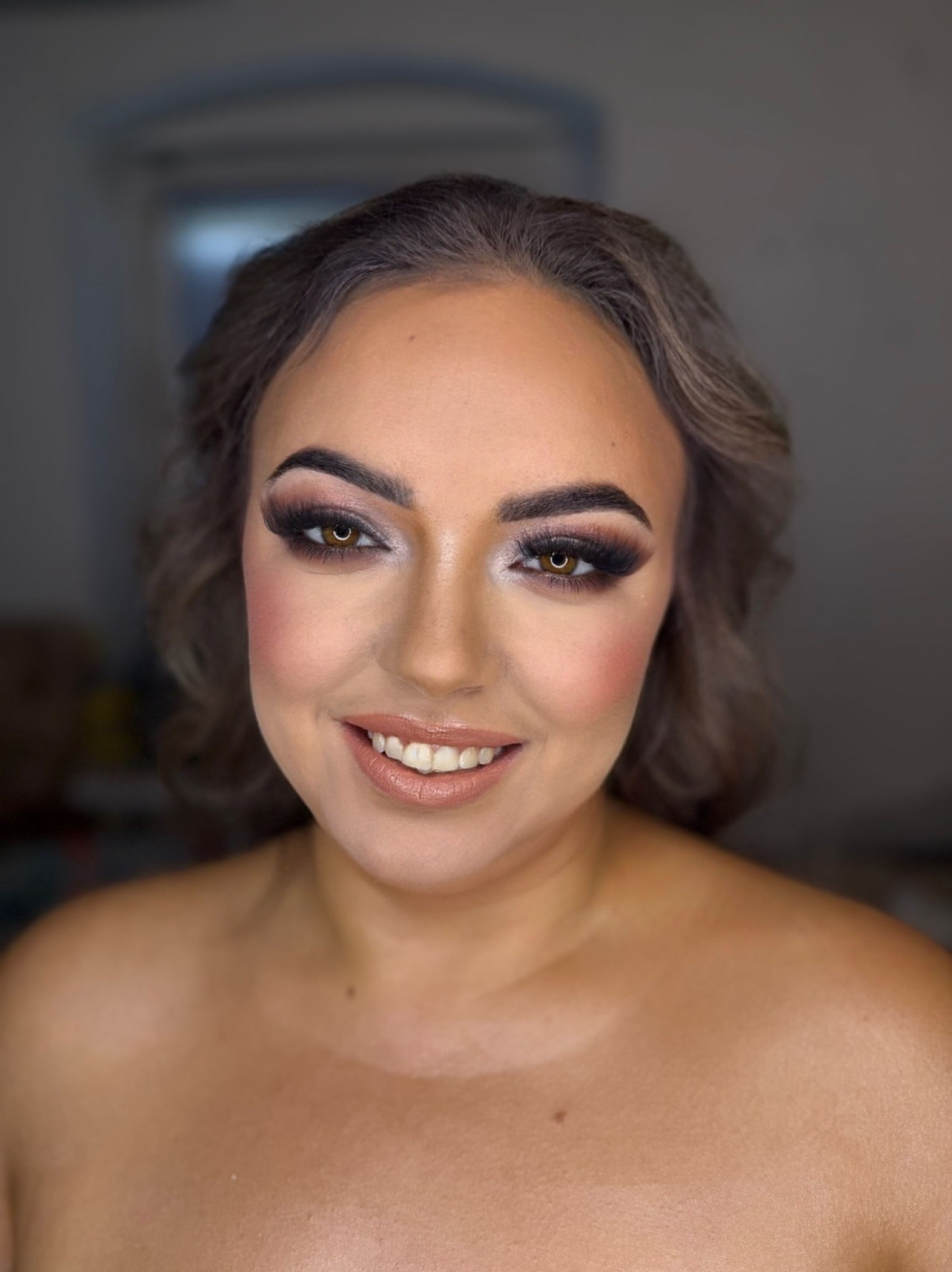 Portret kobiety z profesjonalnym makijażem wieczorowym: wyraziste smoky eyes, podkreślone kości policzkowe, nude usta i delikatne fale. Subtelne oświetlenie.