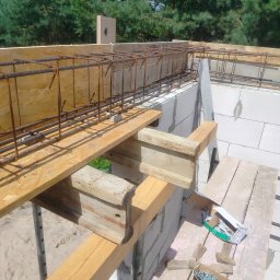 UR-BUD PIOTR URBAN - Zbrojenie fundamentów z betonu komórkowego, widoczne drewniane podpory i narzędzia. Ujęcie z góry na tle zieleni.