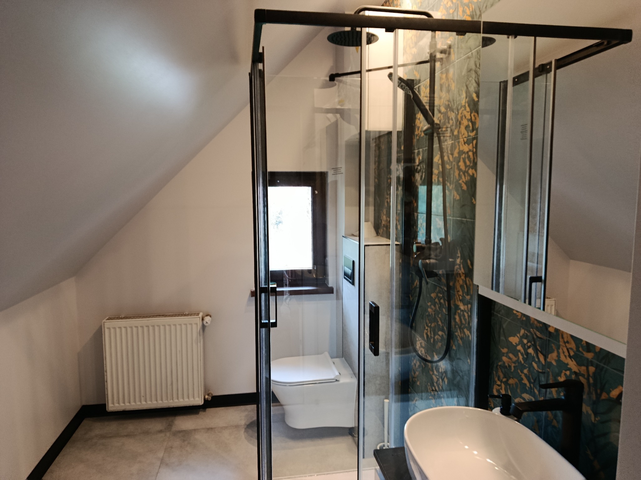 Wykończona łazienka na poddaszu w Łodygowicach. Kabina prysznicowa typu walk-in z czarnymi profilami, umywalka nablatowa i toaleta podwieszana.