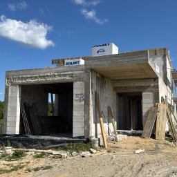KOW-BUD - Niedokończony dom z betonu komórkowego Solbet w słoneczny dzień. Widoczne szalunki, rusztowania i materiały budowlane. Etap budowy w stanie surowym otwartym.