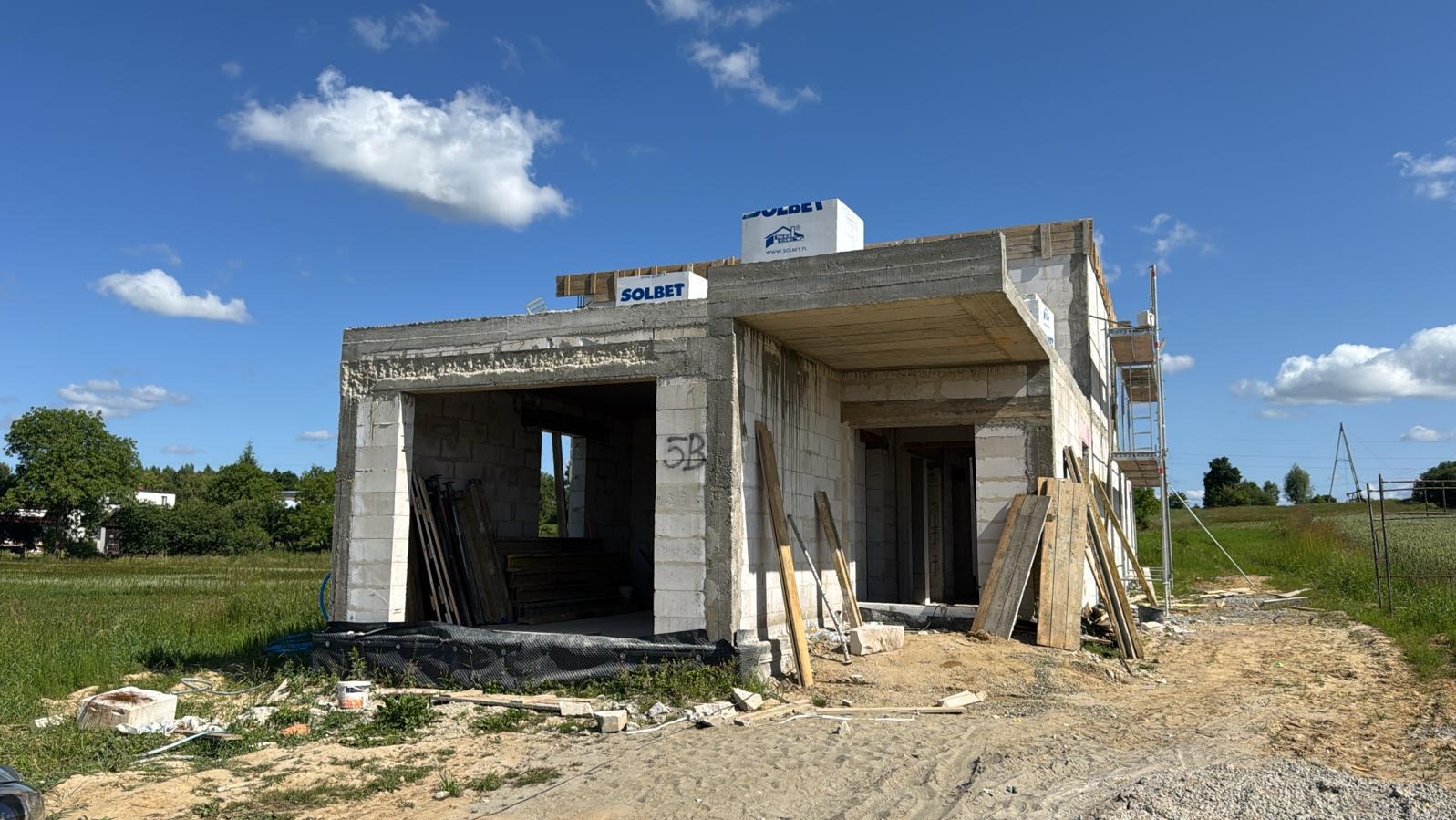 Niedokończony dom z betonu komórkowego Solbet w słoneczny dzień. Widoczne szalunki, rusztowania i materiały budowlane. Etap budowy w stanie surowym otwartym.
