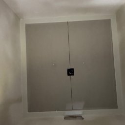 Krzysztof Wielgat - Zamknięte, dwuskrzydłowe drzwi rewizyjne w jasnej obudowie, widoczne od dołu. Na środku widoczny otwór na zamek. Minimalistyczny design.