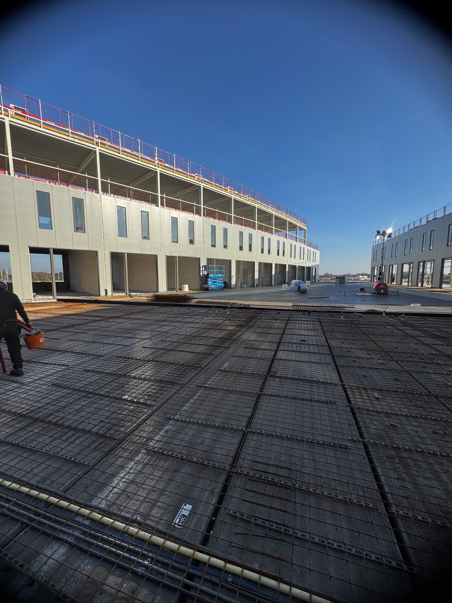 Zbrojenie pod wylewkę na budowie, widoczne budynki w stanie surowym otwartym, błękitne niebo. Prace przygotowawcze do montażu okien i drzwi.