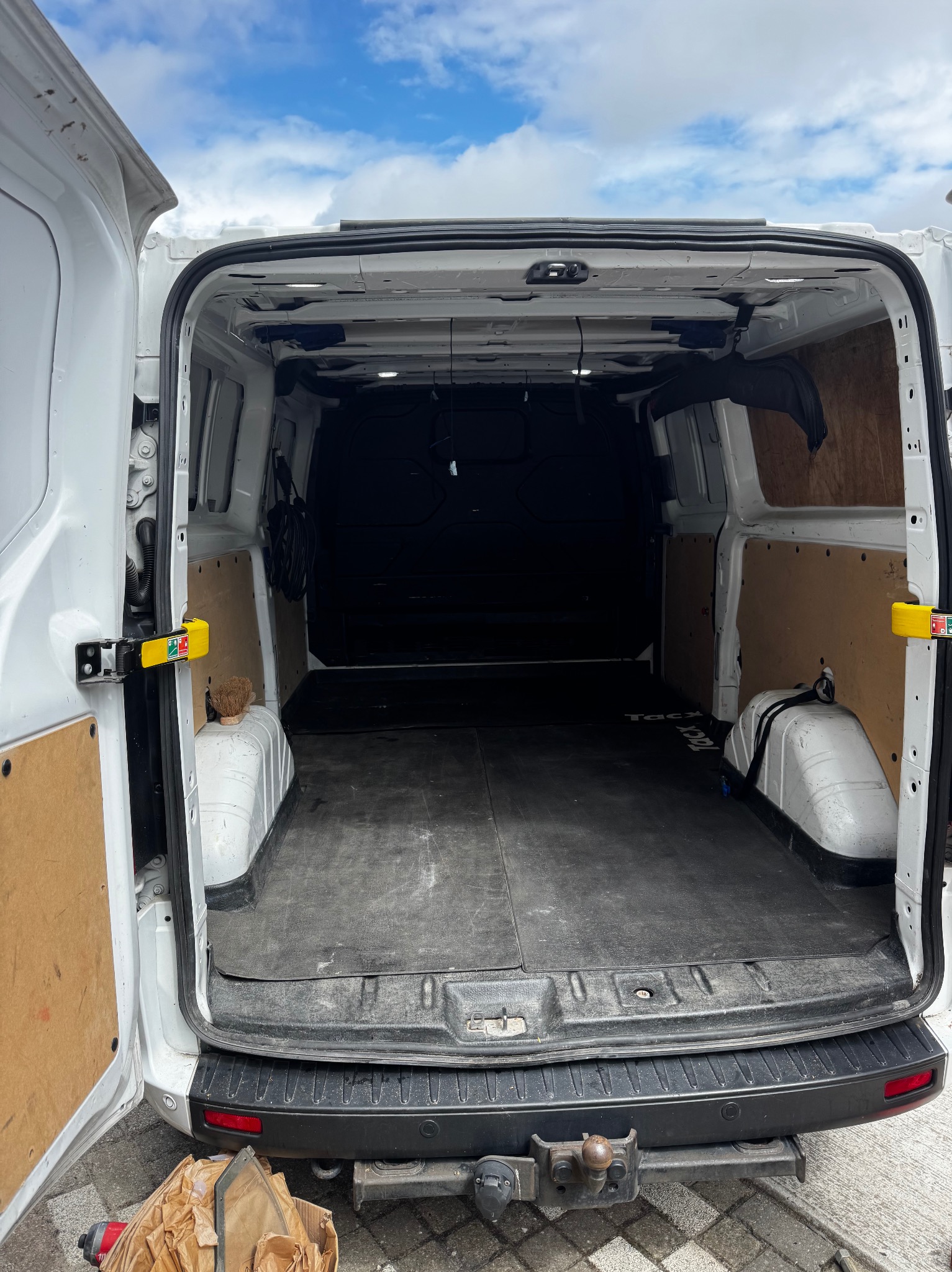 Wnętrze białego furgonetki z otwartymi drzwiami, widok z tyłu, z elementami wyposażenia i narzędziami, sugerujące przygotowanie do transportu okien lub drzwi.