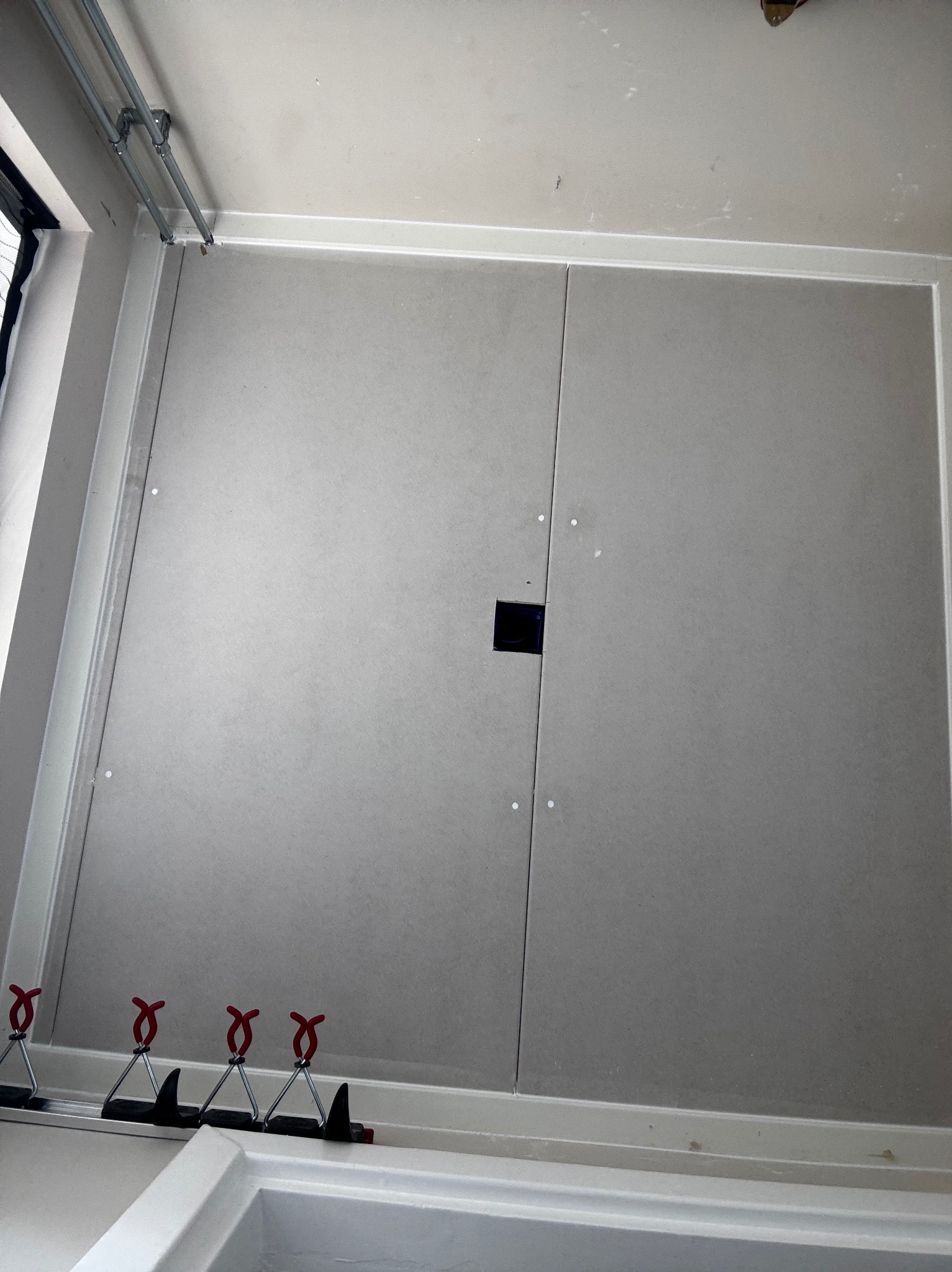 Montaż płyt gipsowo-kartonowych na ścianie z widocznym otworem i narzędziami mocującymi, ukazujący etap prac wykończeniowych w pomieszczeniu.