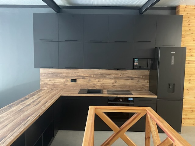 Nowoczesna kuchnia na wymiar z czarnymi frontami i drewnianym blatem. Uwagę przykuwa minimalistyczny design i funkcjonalne rozmieszczenie sprzętów.