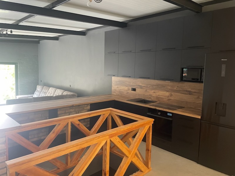 Nowoczesna kuchnia z czarnymi szafkami i drewnianym blatem, widok z antresoli z drewnianą balustradą. Minimalistyczny design, oświetlenie sufitowe.