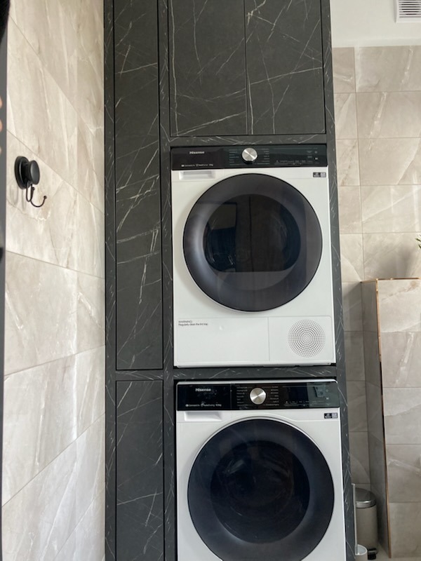 Pralka i suszarka w zabudowie z czarnego marmuru, dopasowane do płytek w łazience. Minimalistyczny design, nowoczesne rozwiązanie do małej przestrzeni.