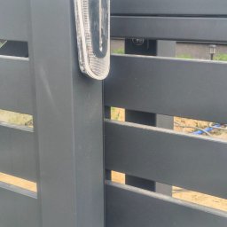 Usługi Ogólnobudowlane Stal-Pro - Szczegółowe ujęcie nowoczesnej, poziomej, metalowej bramy w kolorze grafitowym z lampą ostrzegawczą. Widoczne elementy konstrukcyjne i detale wykończenia.