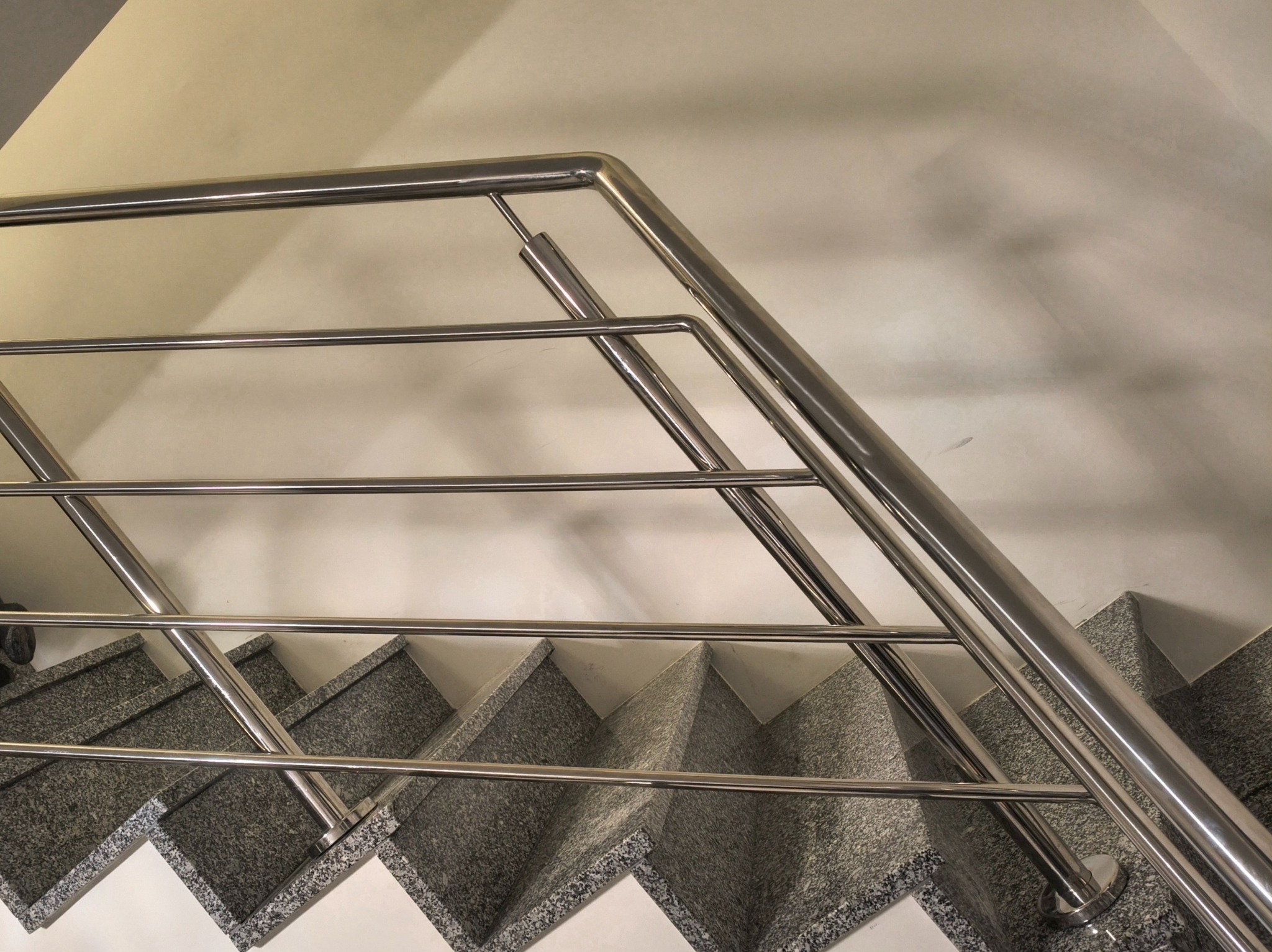 Nowoczesne, metalowe poręcze schodowe z polerowanej stali nierdzewnej, zamontowane na schodach z szarego granitu. Minimalistyczny design, jasne tło.