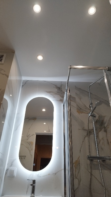 Nowoczesna łazienka z marmurowymi płytkami, podświetlanym lustrem i kabiną prysznicową ze srebrnymi elementami. Widok z dołu, oświetlenie punktowe.