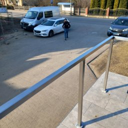 Metalsystem Barbara Brzezińska - Nowoczesna, prosta, metalowa barierka na schodach zewnętrznych, z widokiem na podjazd i ulicę w słoneczny dzień. Minimalistyczny design, szare płytki.