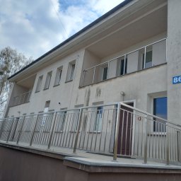 Metalsystem Barbara Brzezińska - Dwukondygnacyjny budynek z balkonami zabezpieczonymi nowoczesnymi, metalowymi barierkami. Ujęcie z dołu, widoczne niebo z chmurami.