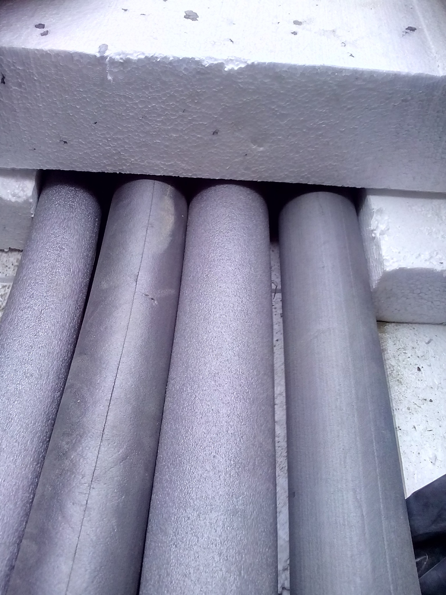 Izolowane rury grzewcze, zabezpieczone styropianem, ułożone równolegle. Widoczne detale struktury izolacji i styropianu.