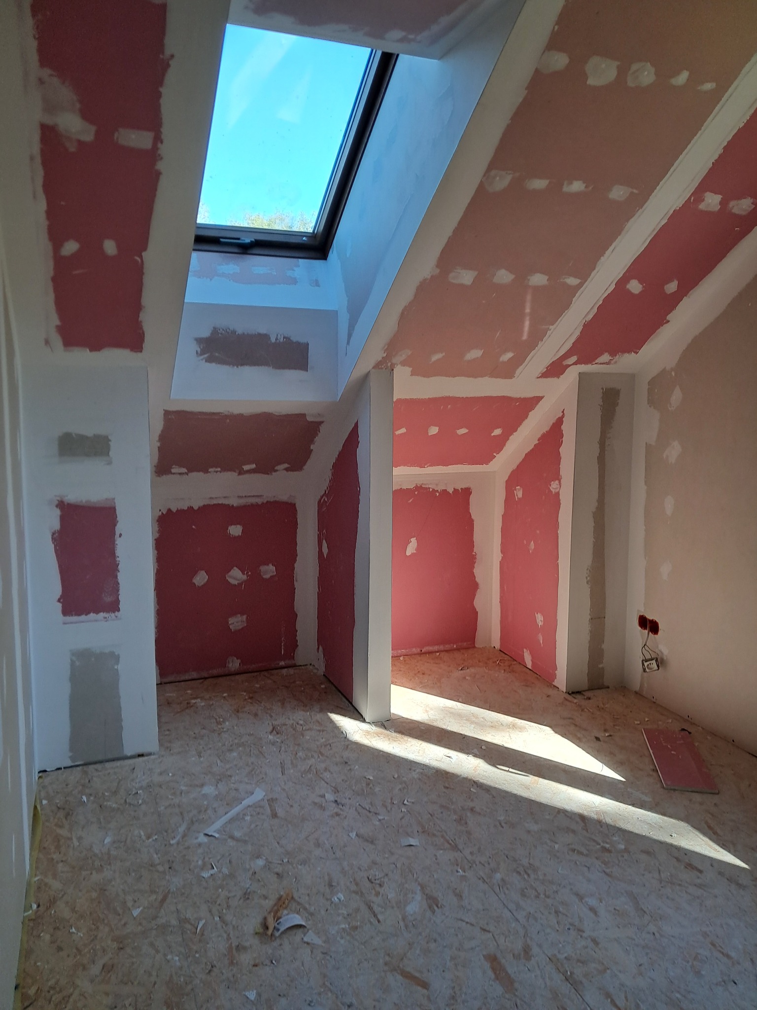 Pokój na poddaszu w trakcie prac wykończeniowych: płyty gipsowo-kartonowe na ścianach i suficie, okno dachowe wpuszczające światło, podłoga z płyt OSB.