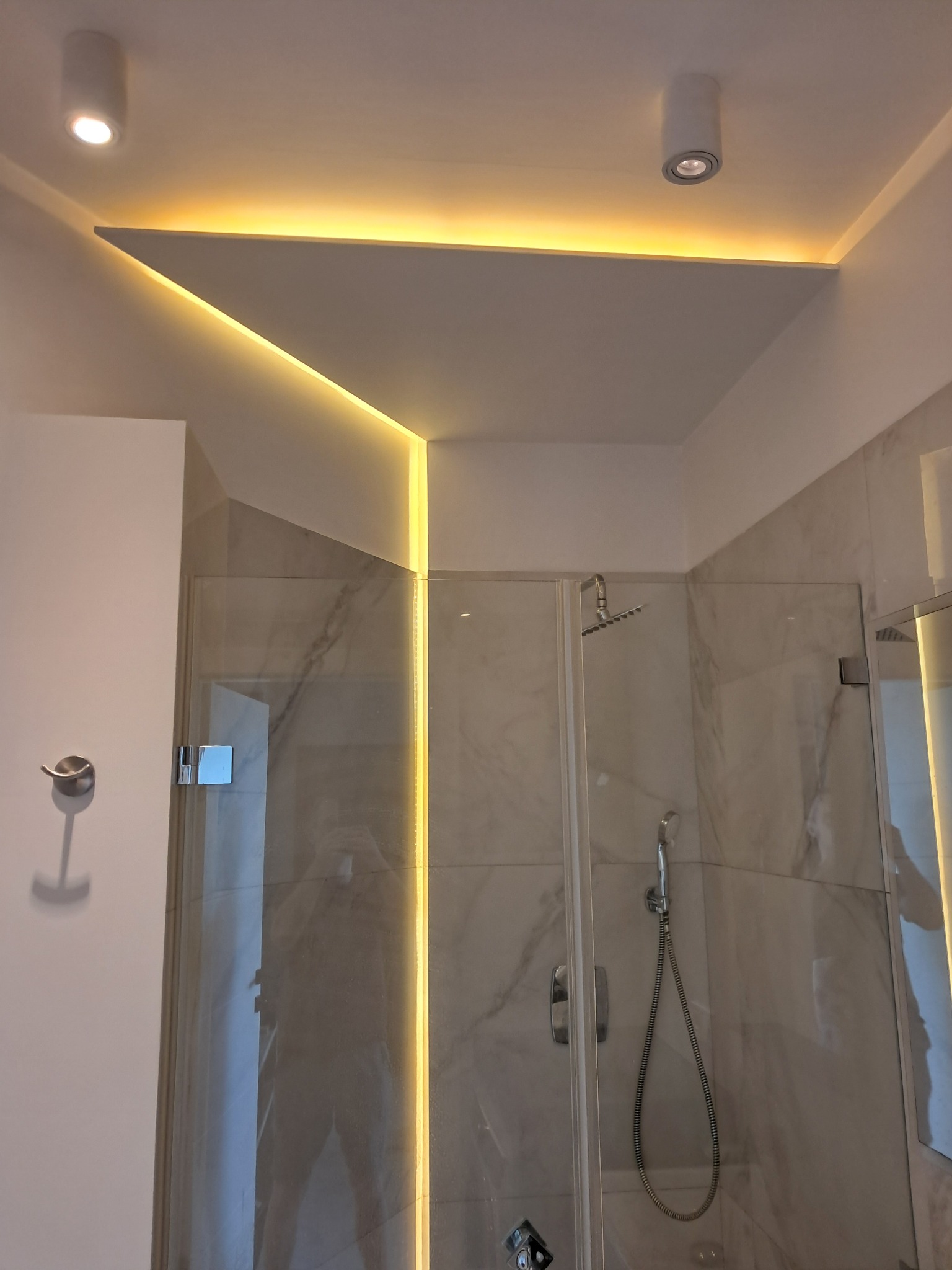 Nowoczesna łazienka z kabiną prysznicową i podwieszanym sufitem z oświetleniem LED. Marmurowe płytki na ścianach. Minimalistyczny design.