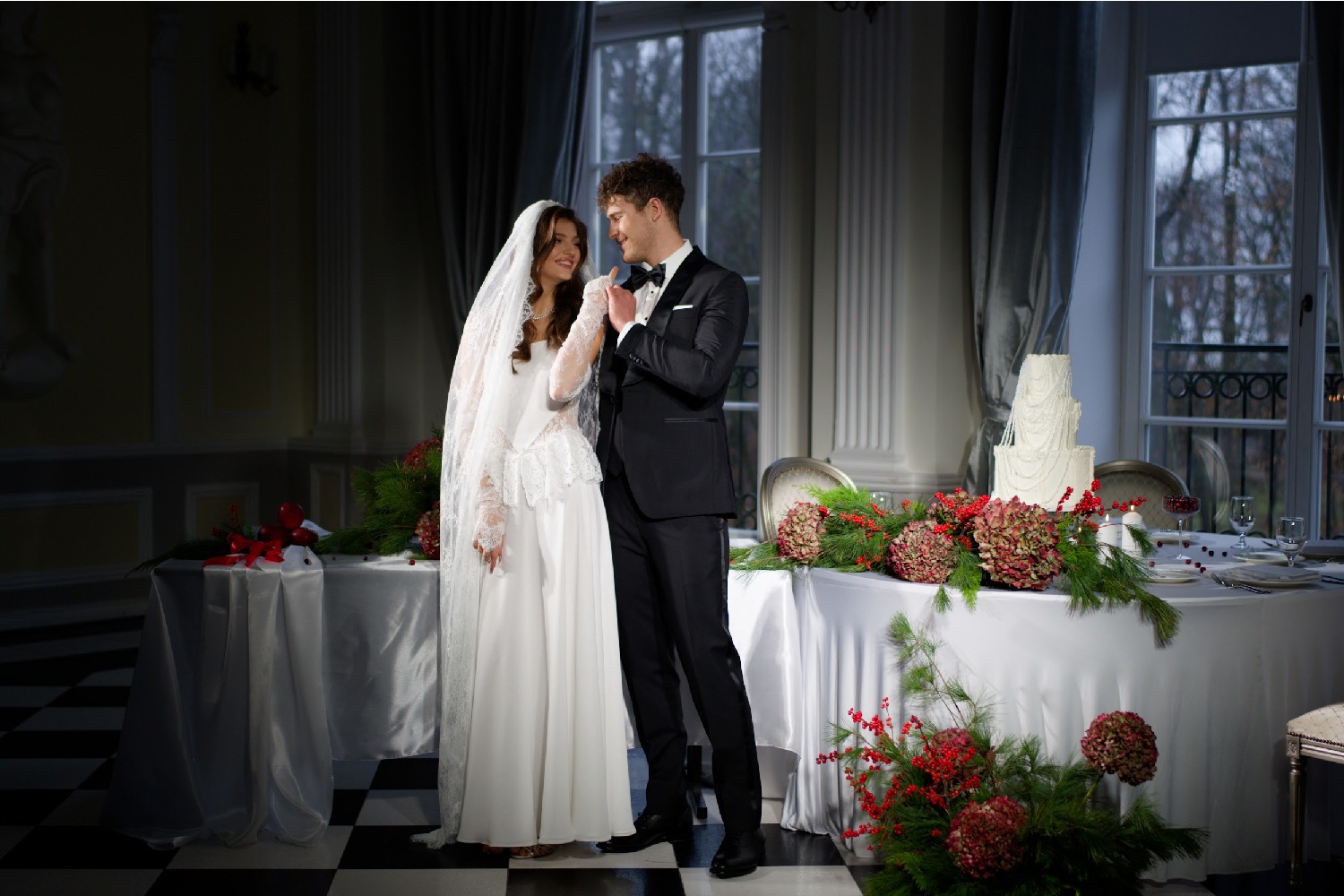 Para młoda w eleganckim pałacu Alexandrinum, obok stołu weselnego z tortem i dekoracjami kwiatowymi. Uśmiechnięci, wpatrzeni w siebie.