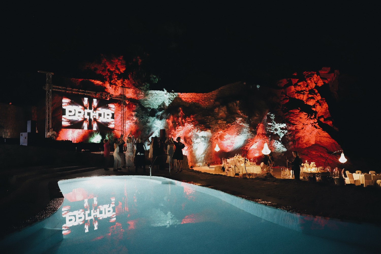 Nocny event firmowy w Dubrowniku: podświetlona skała, basen z odbiciem logo, eleganckie stoły i bawiący się goście tworzą unikalną atmosferę.