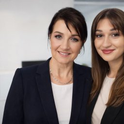 JAGIMO Sp. z o.o. - Uśmiechnięte, profesjonalne kobiety w biurowych strojach, stojące obok siebie na tle jasnego biura. Widoczne detale biżuterii i makijażu.