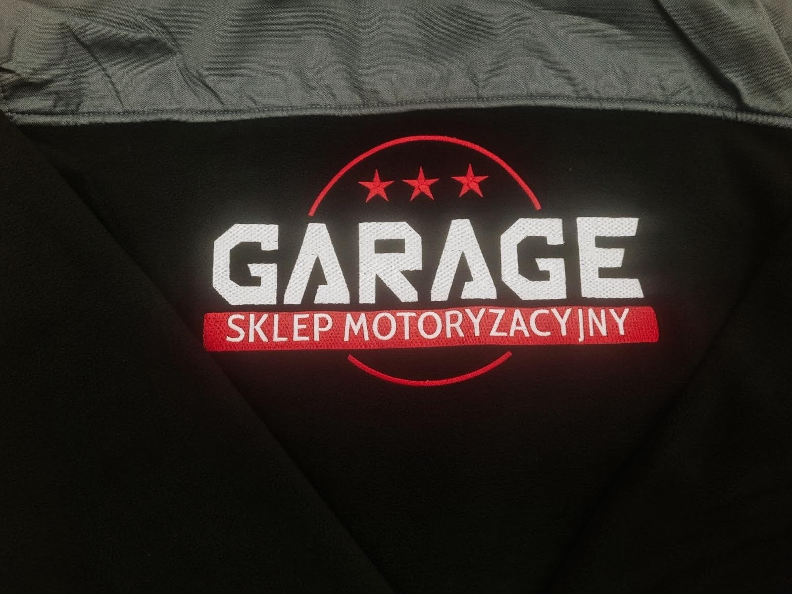 Czarna bluza z wyhaftowanym białym napisem 'GARAGE' i czerwonym 'SKLEP MOTORYZACYJNY' pod spodem, otoczonym czerwonym okręgiem z trzema gwiazdkami u góry.