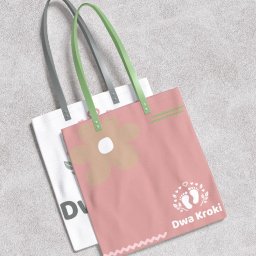 Spójnia Studio Dariusz Kawalec - Dwie torby bawełniane z nadrukiem: biała z inicjałami i różowa z kwiatem i stopkami, leżące na szarym tle. Torby mają uchwyty w kolorze szarym i zielonym.