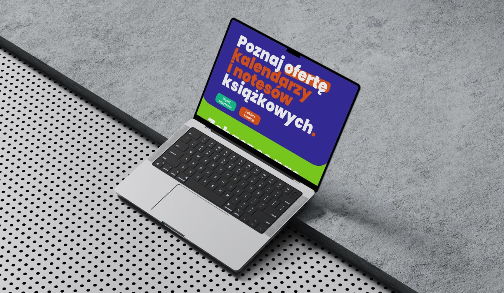 Laptop z wyświetloną ofertą kalendarzy i notesów książkowych na ekranie, umieszczony na szarym, teksturowanym tle z perforowaną powierzchnią.