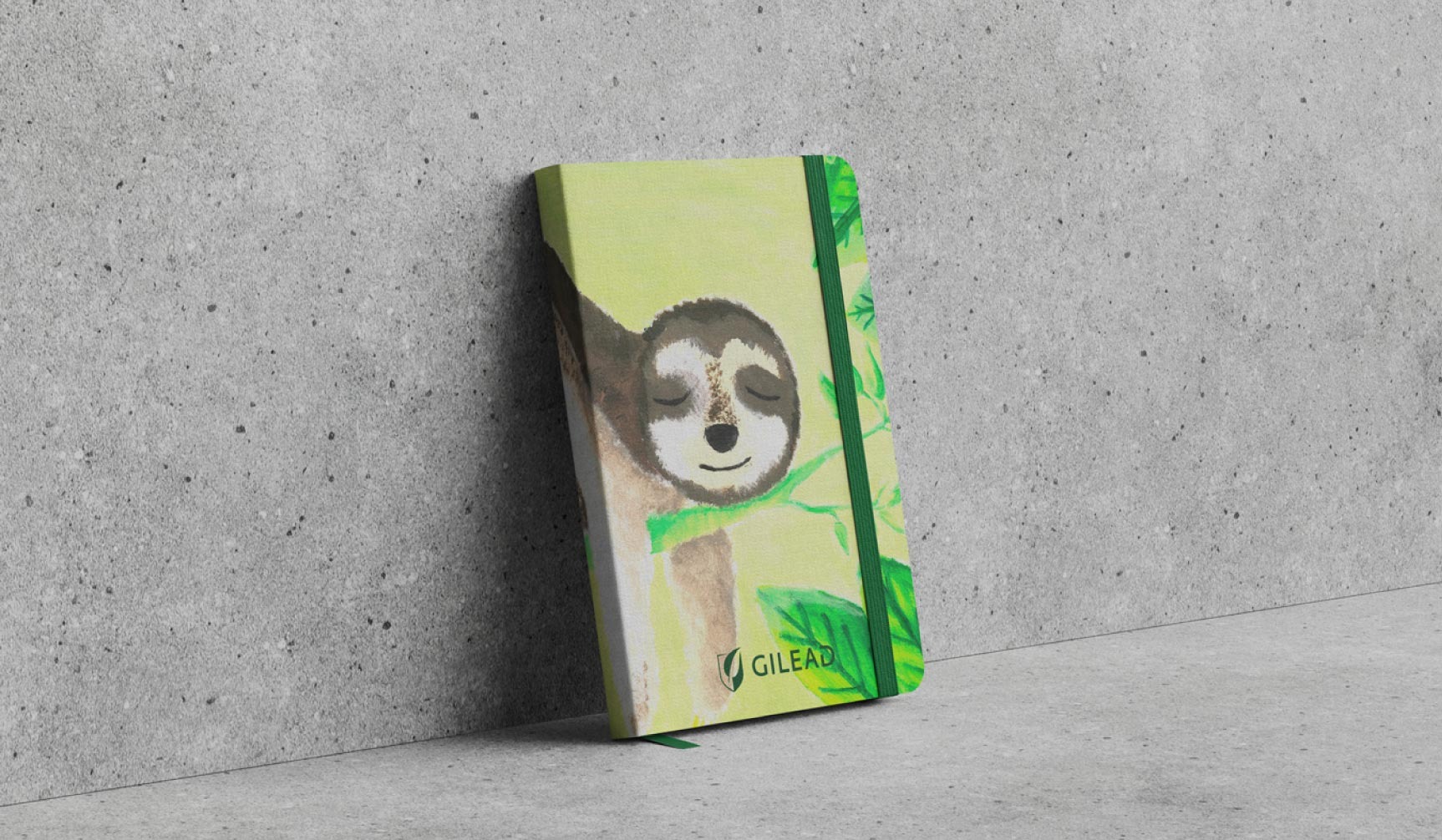 Notatnik z ilustracją leniwca na okładce, oparty o szarą ścianę. Zeszyt ma zieloną gumkę i zakładkę. Widoczne logo firmy Gilead.