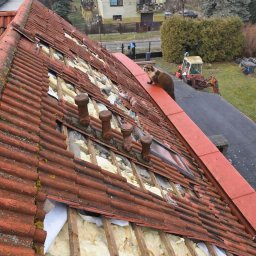 BudMar - Ocieplenie dachu z widoczną izolacją i częściowo zdjętą dachówką. Na dachu kuna. W tle dom i traktor.