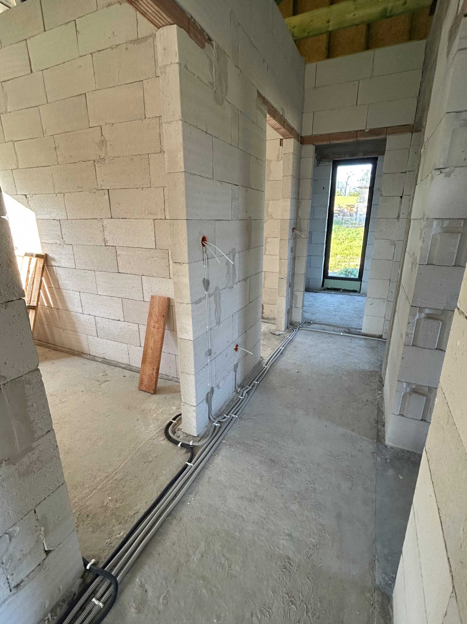 Wnętrze w trakcie budowy z widocznymi przewodami elektrycznymi ułożonymi wzdłuż ściany z betonu komórkowego. Widoczne otwory pod gniazdka i puszki.