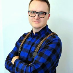 Sanito Paweł Stąsiek - Portret mężczyzny w okularach i niebieskiej koszuli w kratę, z założonymi rękami, na jasnym tle. Widoczne szelki i fragment pasa narzędziowego.