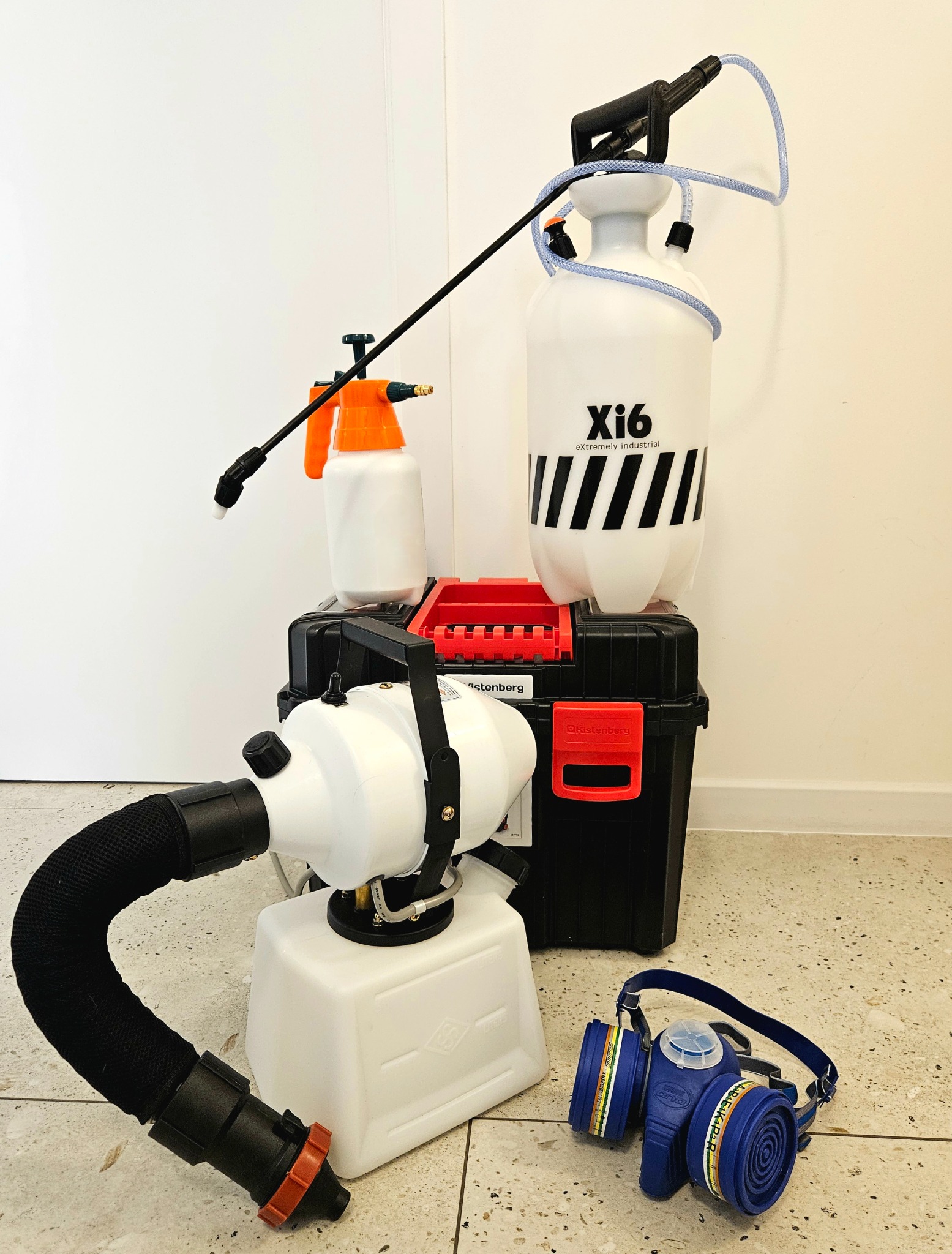 Profesjonalny sprzęt do dezynfekcji: zamgławiacz, opryskiwacze ciśnieniowe i maska ochronna na tle białej ściany i podłogi z płytek.