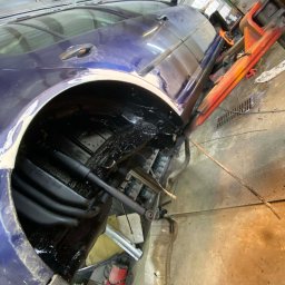 Paint Garage - Niebieski samochód na podnośniku w warsztacie, widoczne podwozie po konserwacji antykorozyjnej, czarna powłoka ochronna. Elementy zawieszenia i podwozia zabezpieczone.