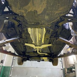 Paint Garage - Podwozie auta po konserwacji antykorozyjnej, widoczne elementy zawieszenia i układu wydechowego. Samochód na podnośniku w warsztacie.