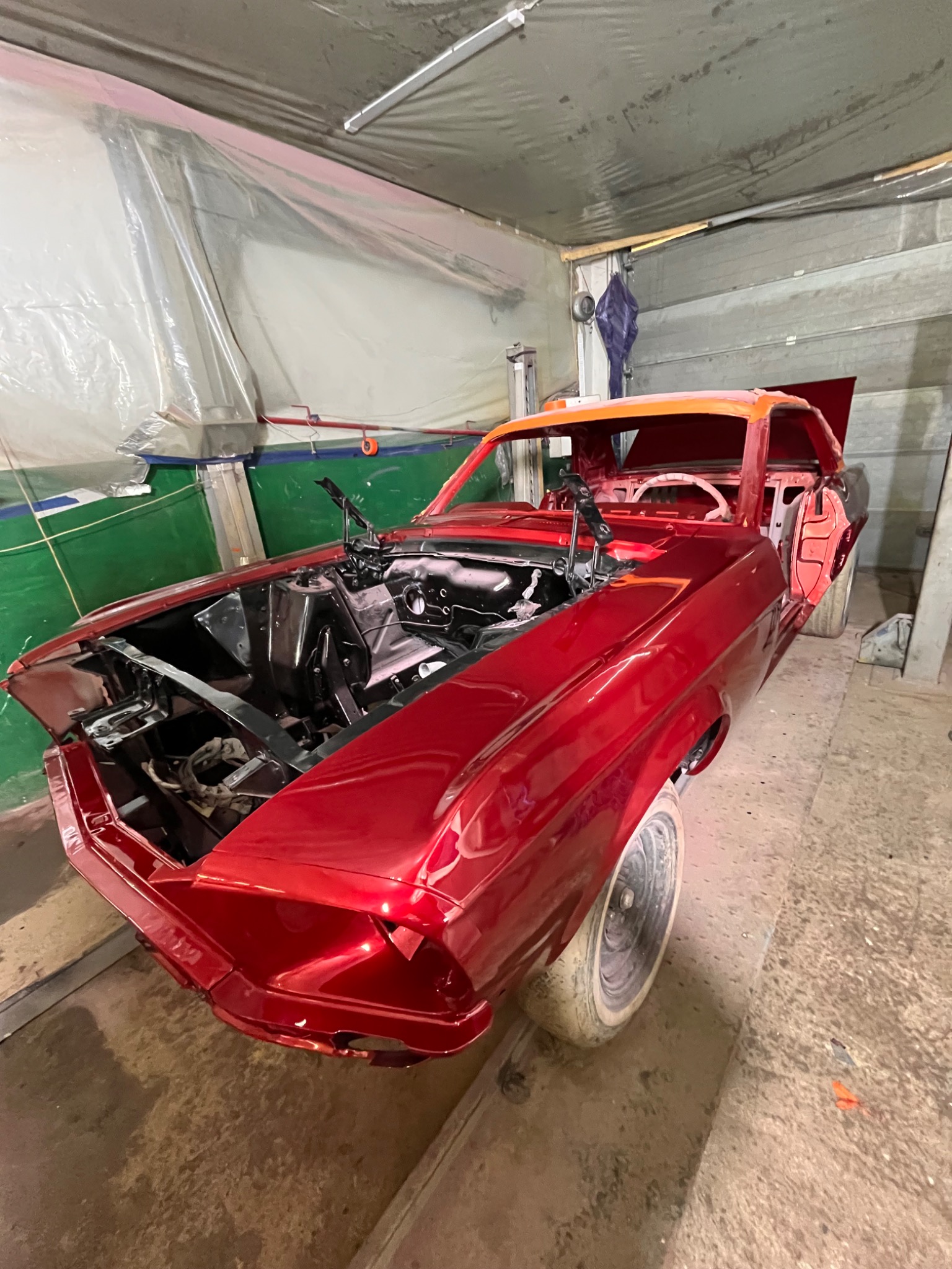 Czerwony, klasyczny Mustang bez maski i z otwartymi drzwiami, w trakcie renowacji w warsztacie. Widoczne elementy karoserii po lakierowaniu.