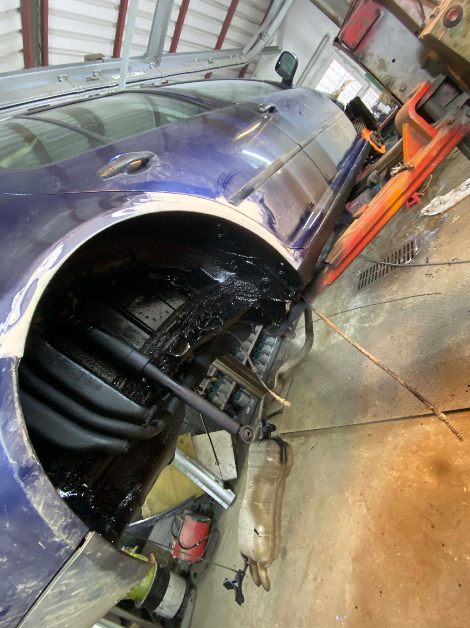 Niebieski samochód na podnośniku w warsztacie, widoczne podwozie po konserwacji antykorozyjnej, czarna powłoka ochronna. Elementy zawieszenia i podwozia zabezpieczone.