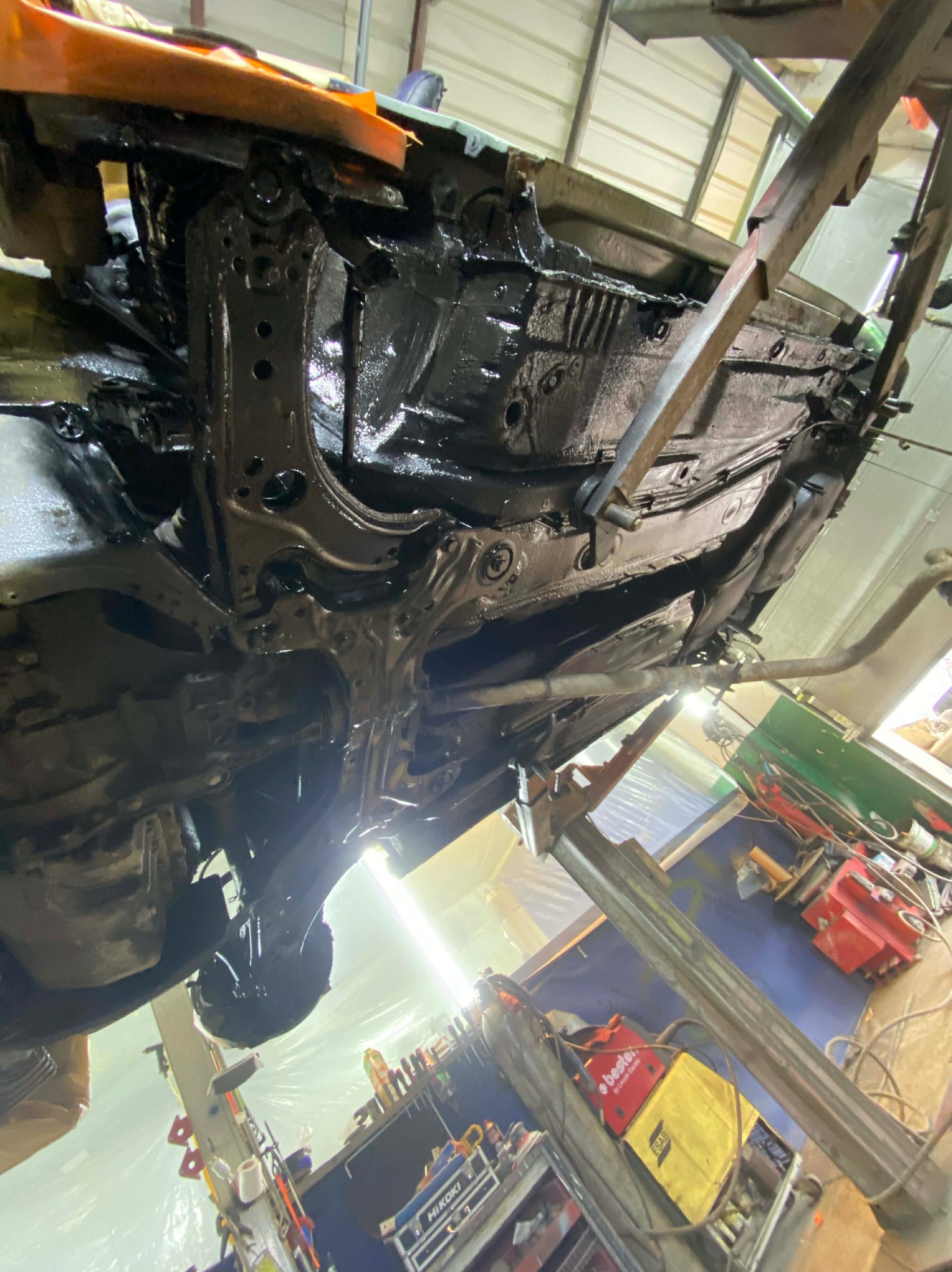 Podwozie samochodu po konserwacji antykorozyjnej, uniesione na podnośniku w warsztacie. Widoczne narzędzia i oświetlenie warsztatowe.