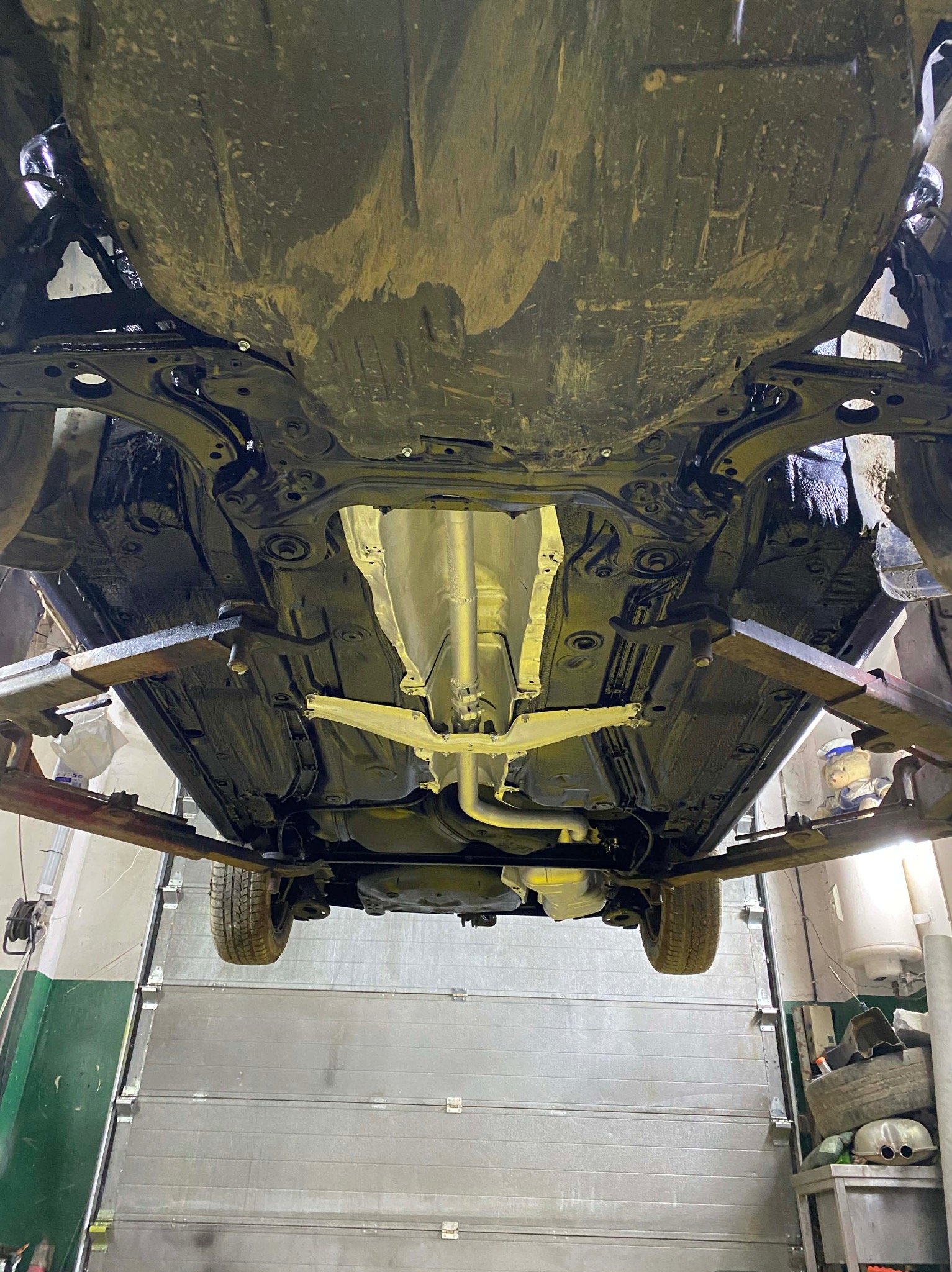 Podwozie auta po konserwacji antykorozyjnej, widoczne elementy zawieszenia i układu wydechowego. Samochód na podnośniku w warsztacie.