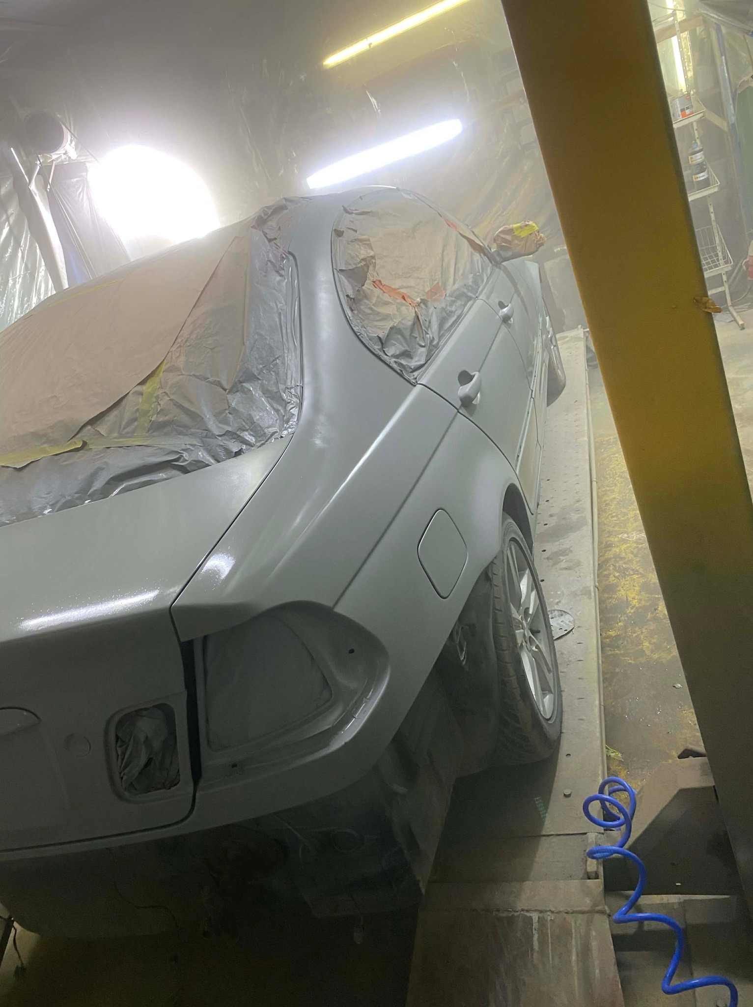Samochód w trakcie lakierowania, częściowo zakryty folią ochronną, widoczny w warsztacie na podnośniku. Świeżo nałożona warstwa lakieru.