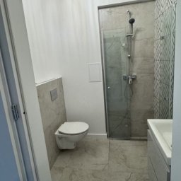 Green Work - Nowoczesna łazienka z kabiną prysznicową, toaletą podwieszaną i umywalką w jasnych odcieniach szarości, wykończona marmurowymi płytkami podłogowymi.