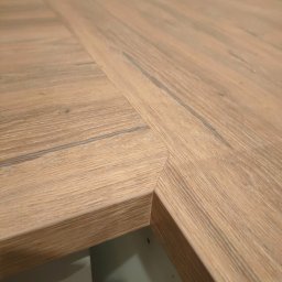 Eniu Design Ernest Borowiak - Połączenie dwóch blatów drewnianych pod kątem, tworzących narożnik. Widoczne usłojenie drewna i precyzyjne wykończenie krawędzi. Blat o ciepłej, naturalnej kolorystyce.