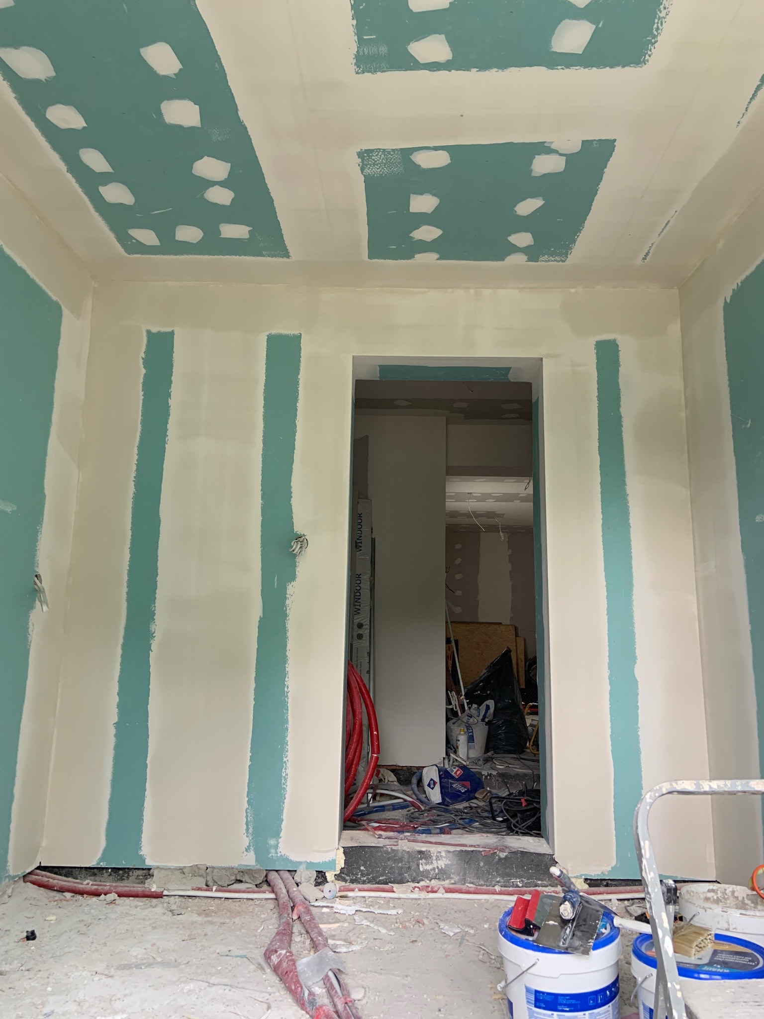 Ściany i sufit w trakcie przygotowania do malowania, z widocznymi fragmentami płyt gipsowo-kartonowych i nałożonymi punktowo łatami szpachli. Widoczne narzędzia i materiały budowlane.