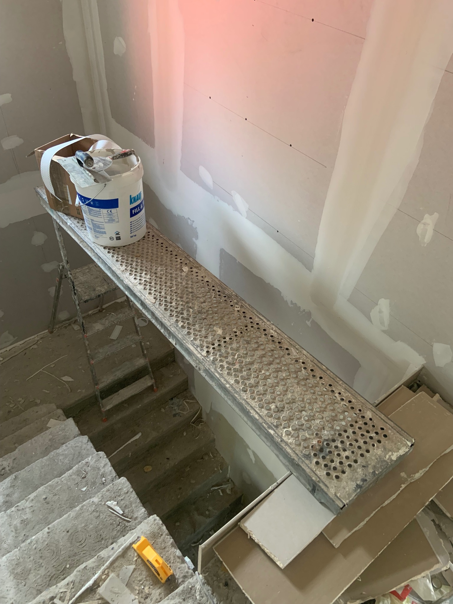 Sufit i ściany po szpachlowaniu, widoczne z rusztowania z wiadrem gładzi Knauf. Schody w remoncie, widok z góry.